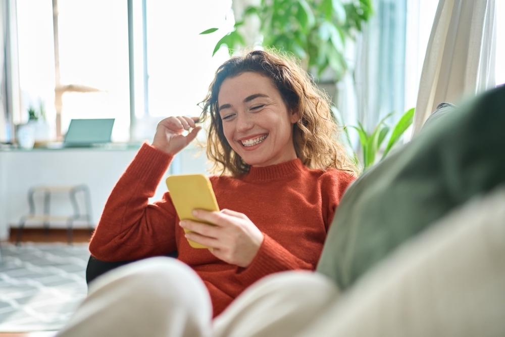 Young woman smiling using her phone in an apartment