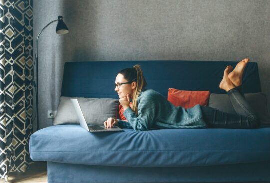 Woman lounging on the couch researching how to rent an apartment.