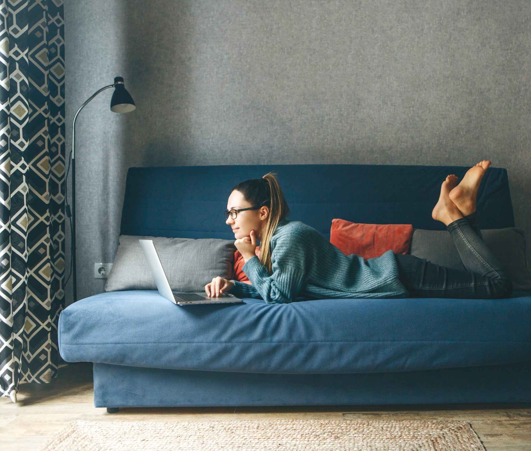 Woman lounging on the couch researching how to rent an apartment.