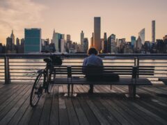 A person sits on a bench overlooking the New York City skyline.