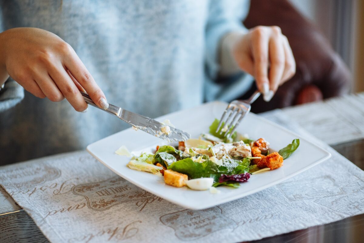 Woman cuts Caesar salad with a fork and knife on a table in one of the best restaurants in LA.