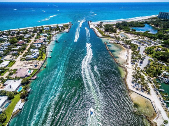 A beautiful day at the beach with boat goers enjoying the beautiful waters. Drone view of the outlet into the beach in West Palm Beach.