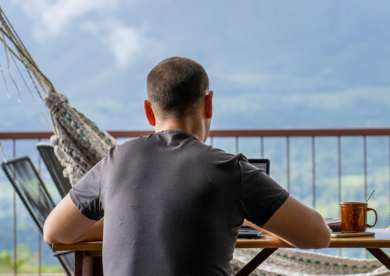 Digital nomad sitting on a table with breakfast while working with a view of a volcano in front of him.