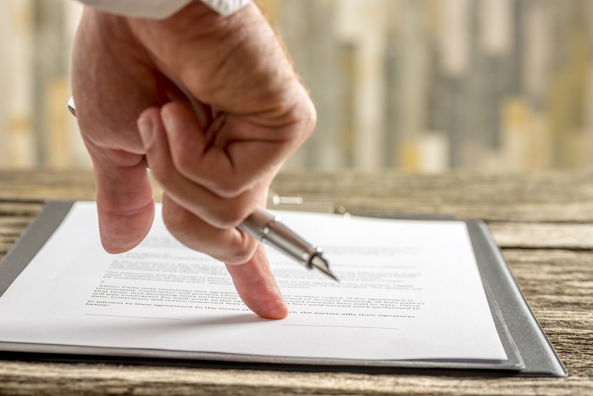 Closeup of hand holding a pen pointing to a line at the end of a lease.