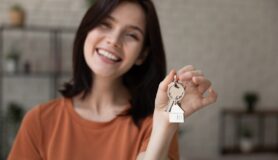 Portrait of happy, laughing millennial woman looking at camera showing key from new rented apartment after negotiating her rent.
