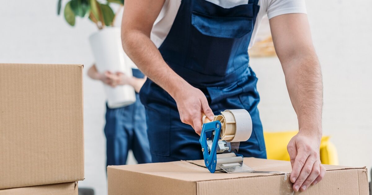 Professional mover wrapping cardboard box with tape in an apartment.