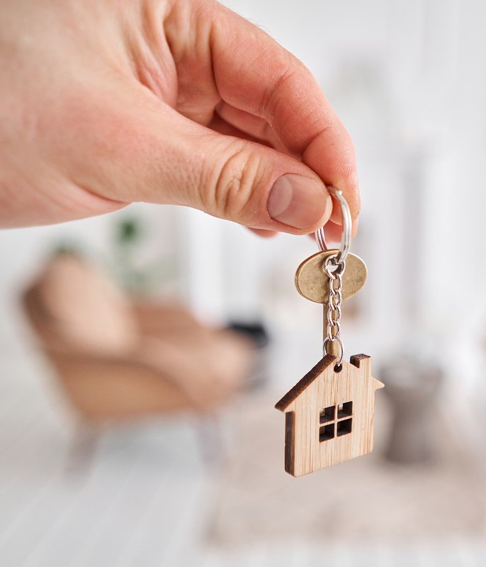 A man’s hand holds a key with a house-shaped keychain.