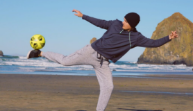 Max Hilty balances a soccer ball on his foot on the beach.