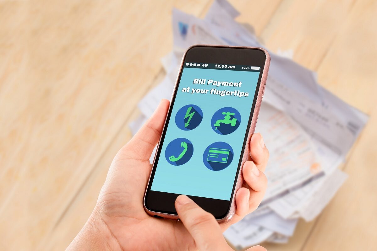 Hands holding smartphone online bill payment at your fingertips with utilities bill on wooden table in background.