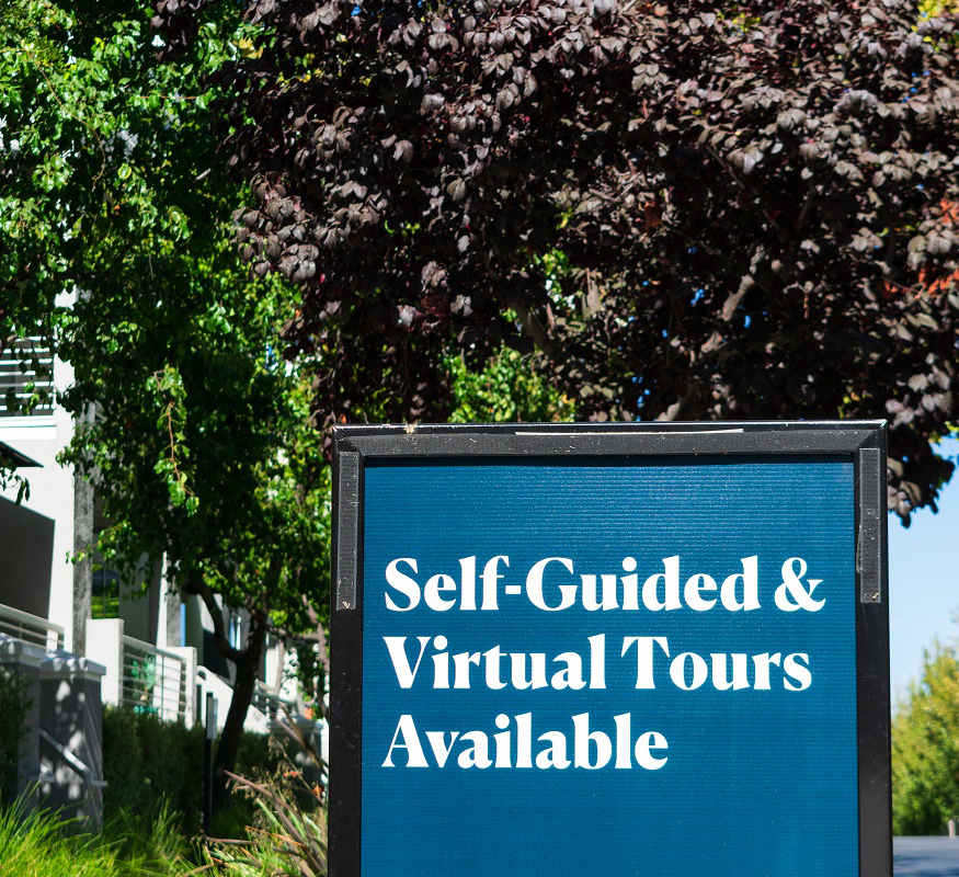 “Self-Guided and Virtual Tours Available” advertisement sign near an apartment building.