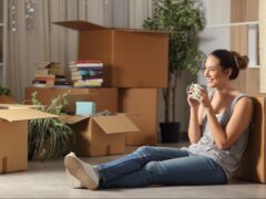 Woman sits in her new apartment surrounded by moving boxes