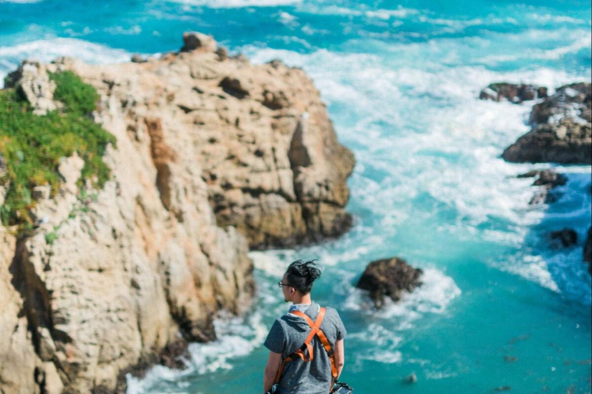 Man stands on a cliff overlooking beautiful blue water.