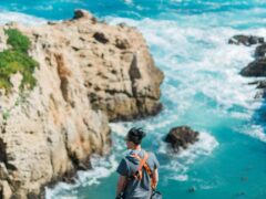 Man stands on a cliff overlooking beautiful blue water.
