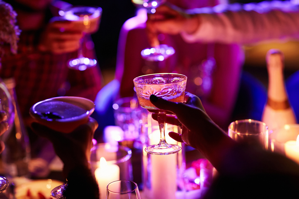 Close up of people drinking cocktails in restaurant. People having good time, cheering and drinking cold cocktails, enjoying friendship together in restaurant, close up view on hands.