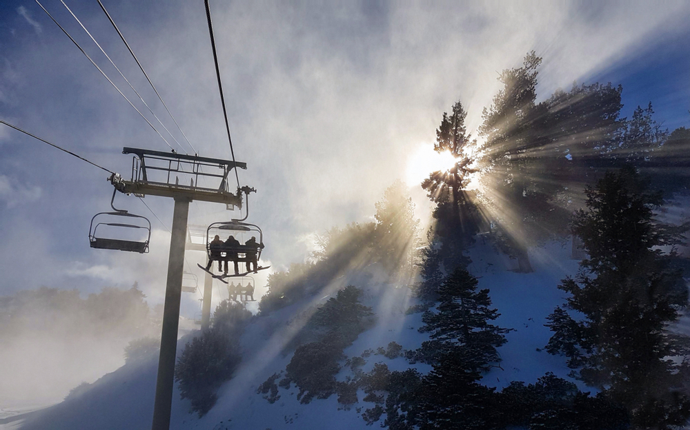 Group of friends on a snowboarding trip to Copper Mountain ride the chairlift through the fog on sunny winter morning. Morning sunbeams shine on snowboarders riding ski lift up to the top of mountain.