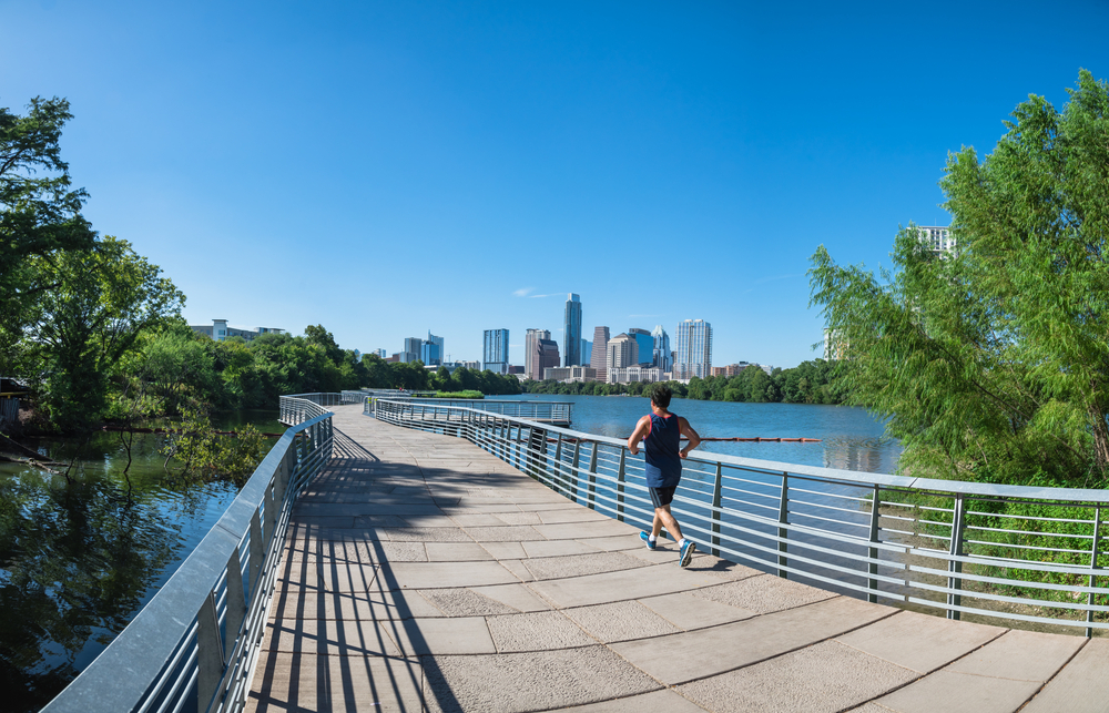 Panorama view Downtown Austin, Texas, US along Colorado River at daytime with cloud blue sky. View from Ann and Roy Butler Hike-and-Bike Trail and boardwalk at Lady Bird Lake, unidentified man running