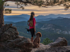 A hispanic woman is hiking with a dog, in the Rocky Mountains, of Colorado.