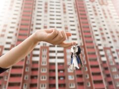Hand holding keys with apartment building in the background