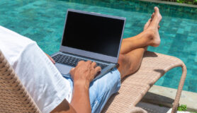 A man uses his laptop by a swimming pool during a workcation.