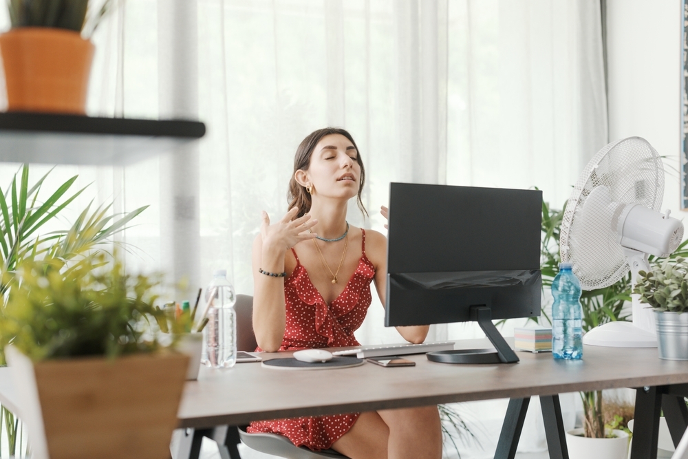 Woman sitting in her apartment on a hot day, cooling down with a fan.