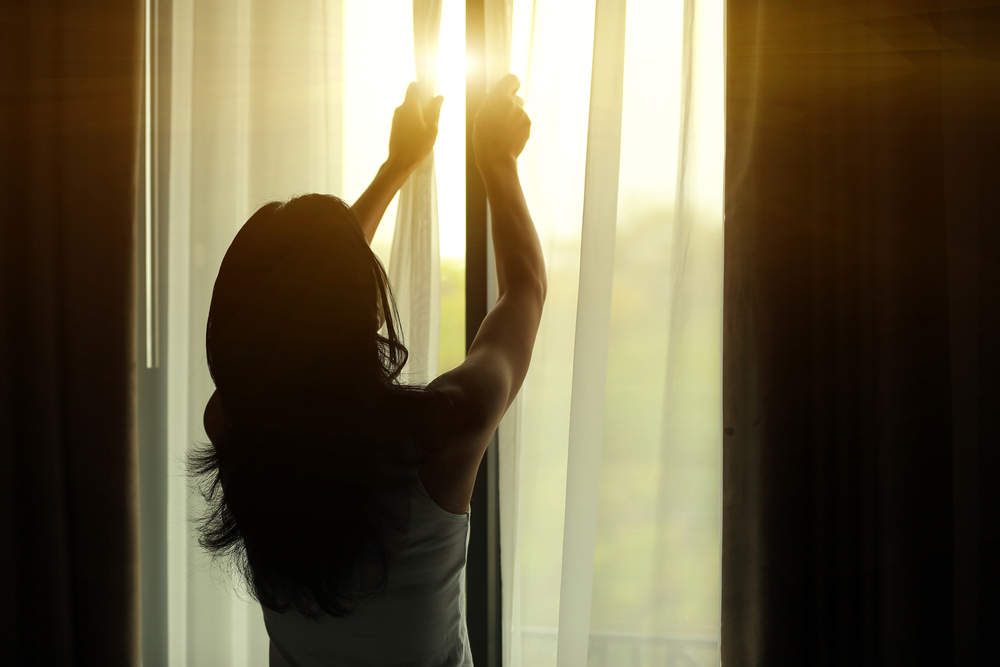  young woman opening curtains in a bedroom