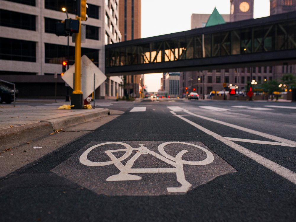 A landscape photo of the bike lane in down town Minneapolis. The photo is taken from the middle of the street with cityscape in the background.