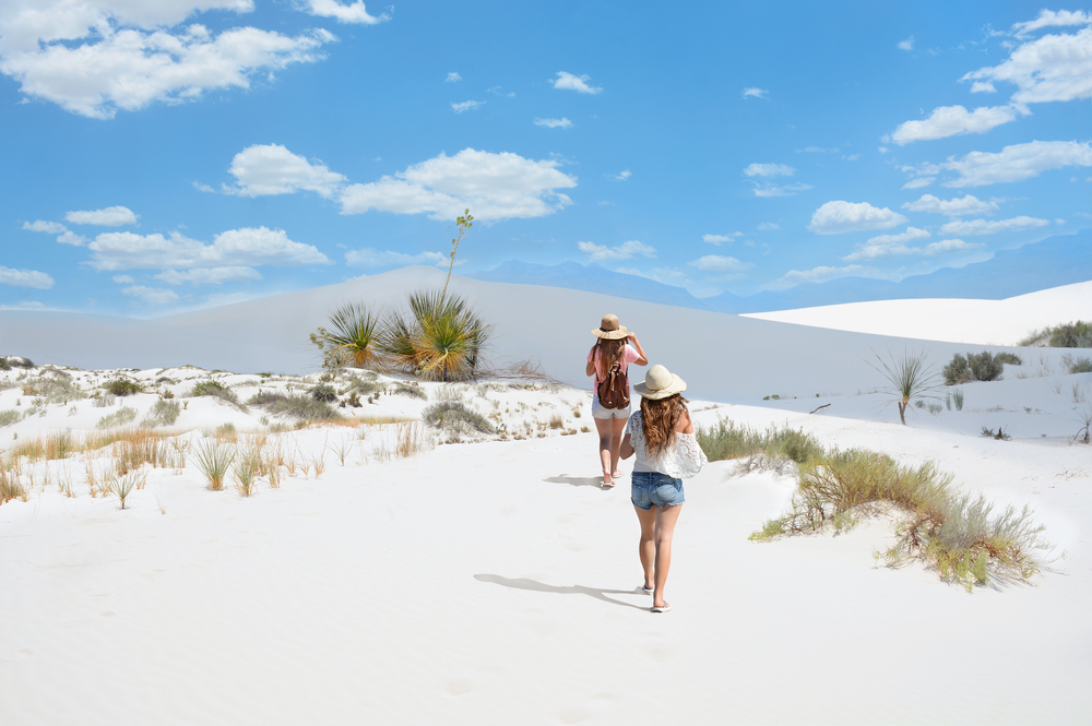 Girls on hiking trip on the mountain desert, Blue sky with clouds in the background. Plants and shrubs growing on sand dunes. White Sands National Monument, New Mexico, USA