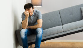 Man sits on couch that's too big for his apartment, one of the top moving mistakes people make.
