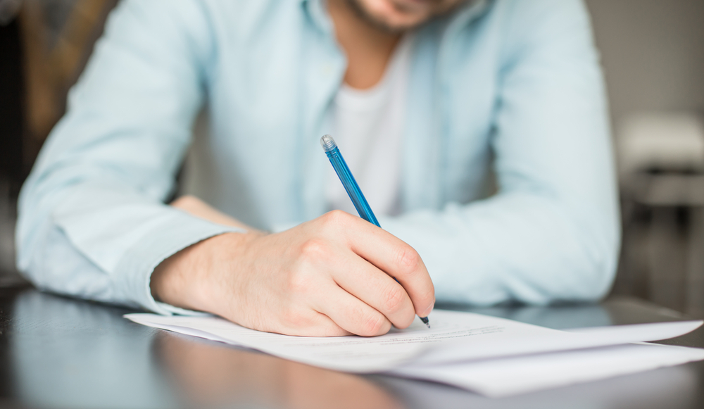 A person's hand holds a pen and writes a rent reduction letter to their landlord.