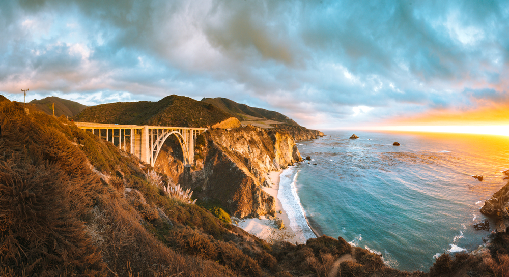 Scenic panoramic view of historic Bixby Creek Bridge along world famous Highway 1 in beautiful golden evening light at sunset with dramatic cloudscape in summer, Monterey County, California, USA