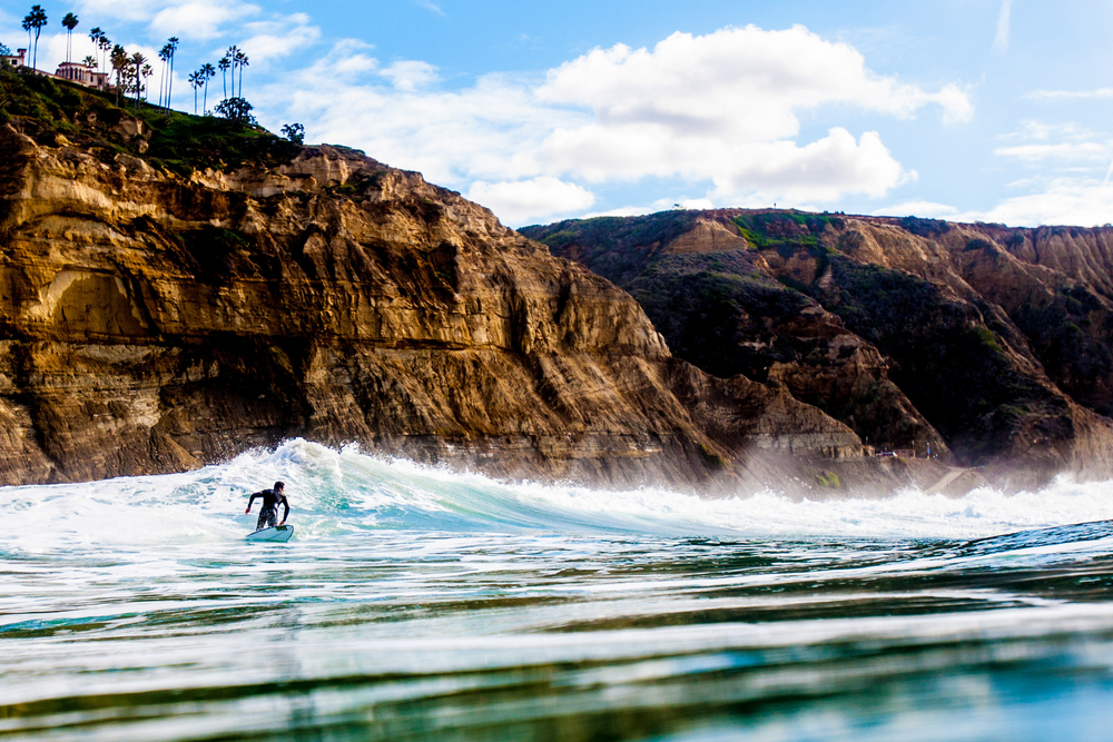 With cliffs towering over him, a surfer pulls out of a wave in San Diego, California.