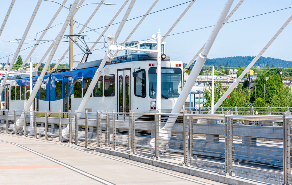 A city public tram with several wagons and a number of windows travels along the Tilikum Crossing Bridge route, transporting Portland residents and visitors to the other side of the Willamette River