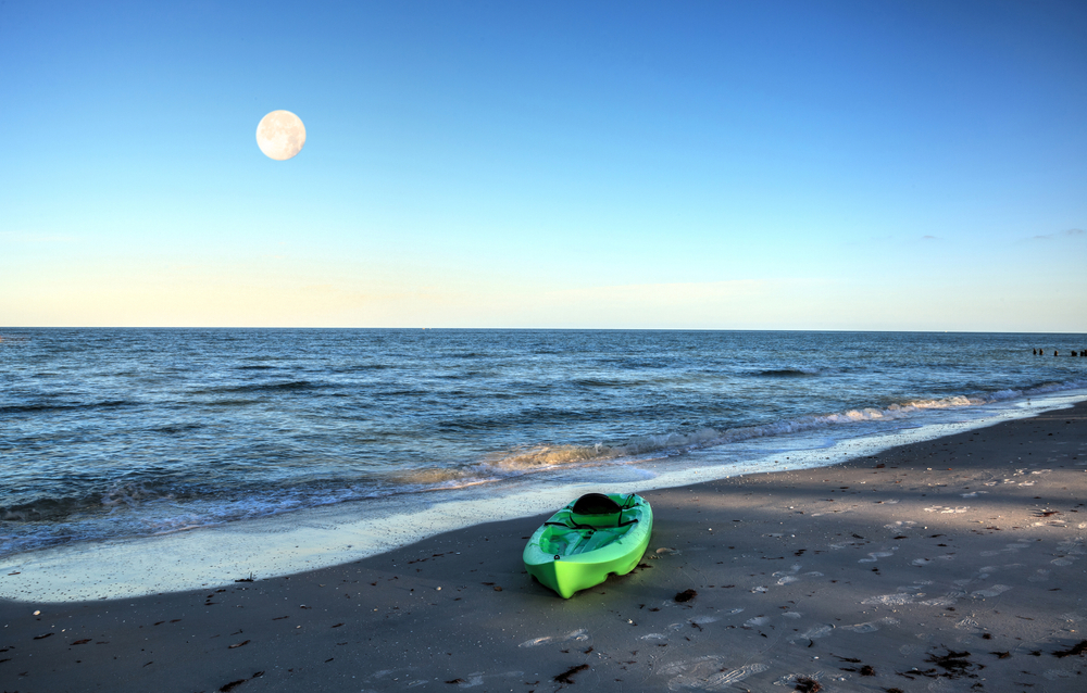 Green kayak on the white sand of Tigertail Beach in Marco Island, Florida as the full moon sets.