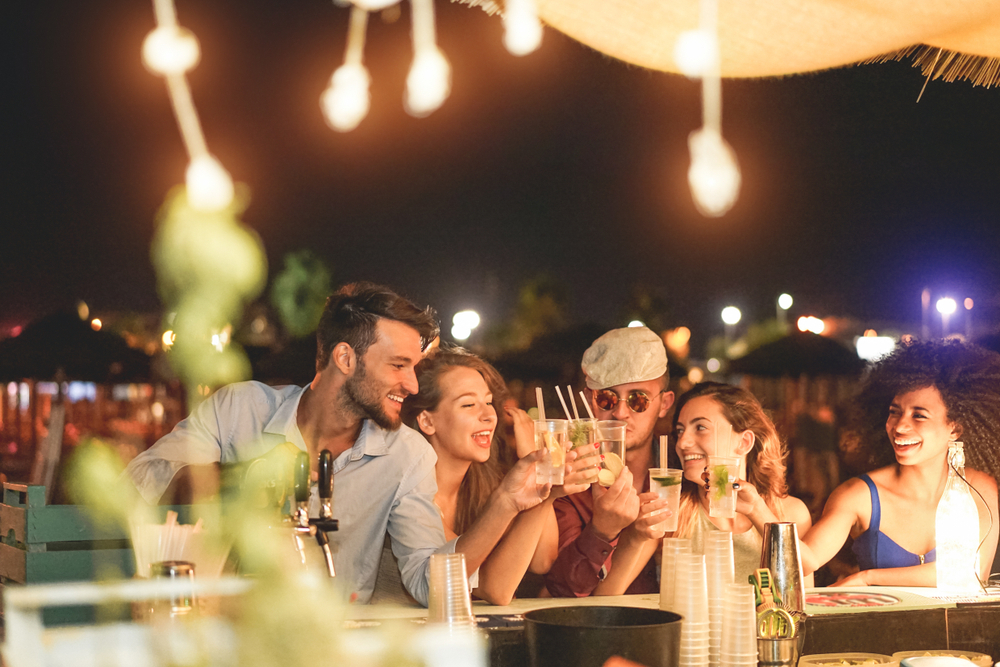 A group of friends raising drinks at an outdoor bar, enjoying the best happy hour deals in Miami.