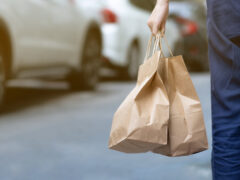 A walking person holds two bags of takeout food