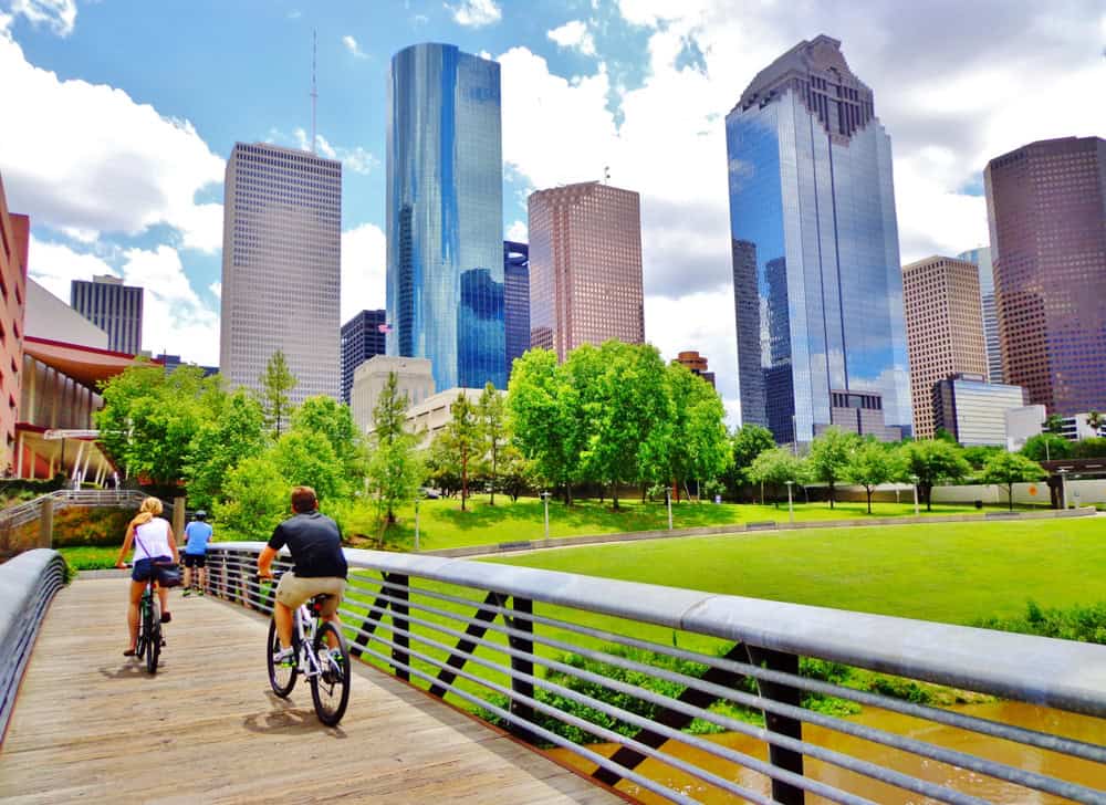 Bicyclists cross wooden bridge in Buffalo Bayou Park, with a beautiful view of downtown Houston (skyline / skyscrapers) in background on a summer day - Houston, Texas, USA 