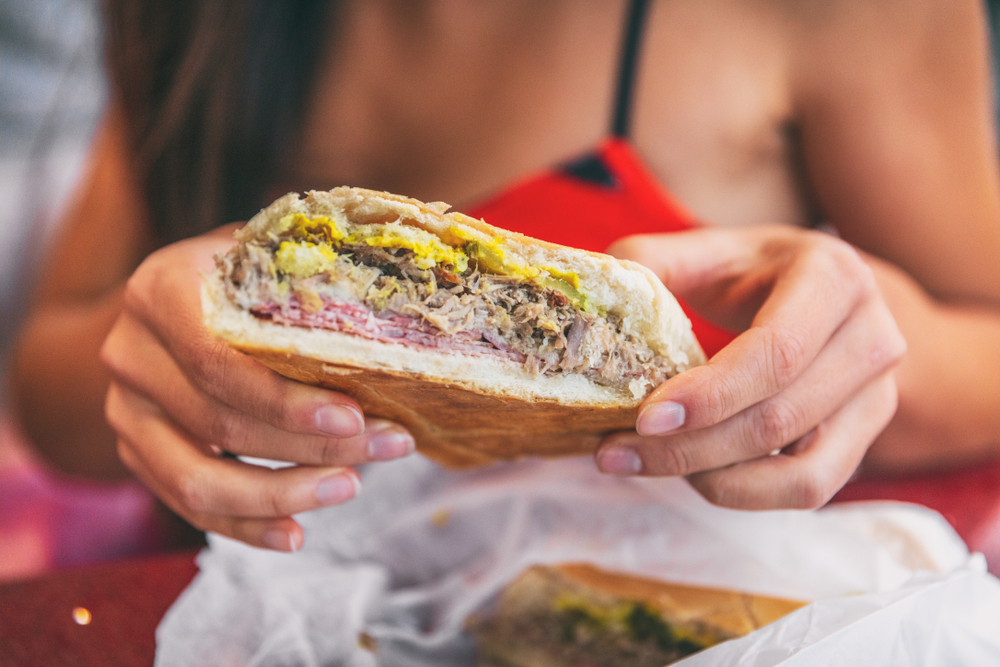 Cuban sandwich closeup woman holding local food at typical cafe outside. Pressed cuban bread with roasted pork, salami sausage, swiss cheese, mustard, typical cuba dish. Cuban sandwich closeup woman holding local food at typical cafe outside. Pressed cuban bread with roasted pork, salami sausage, swiss cheese, mustard, typical cuba dish.