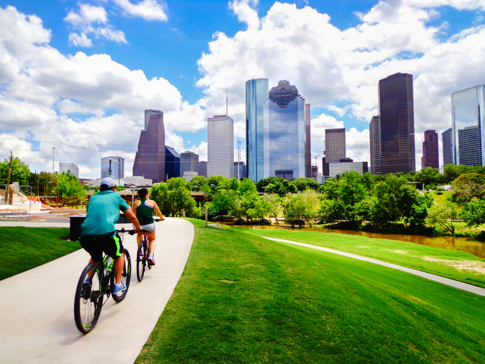 Riding Bikes on Paved Trail in Houston Park (view of river and skyline of downtown Houston) - Houston, Texas, USA Riding Bikes on Paved Trail in Houston Park (view of river and skyline of downtown Houston) - Houston, Texas, USA