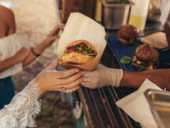 Woman hand reaching for a burger at food truck. Closeup of food truck salesman serving burger to female customer.