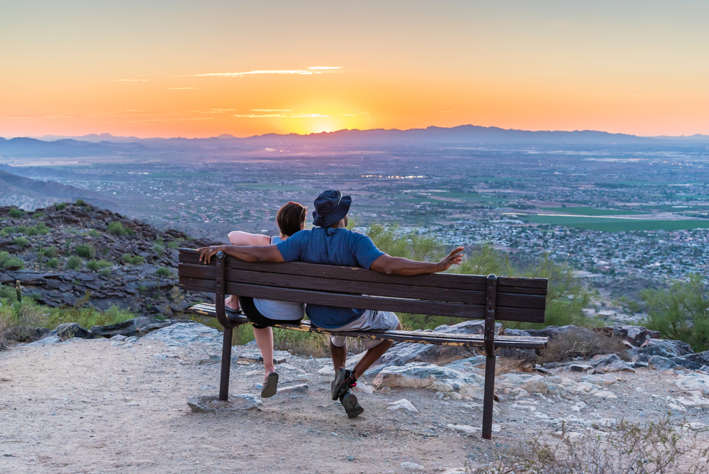 Couple watches from Dobbins Lookout on South Mountain as the sun goes down over Phoenix, Arizona.