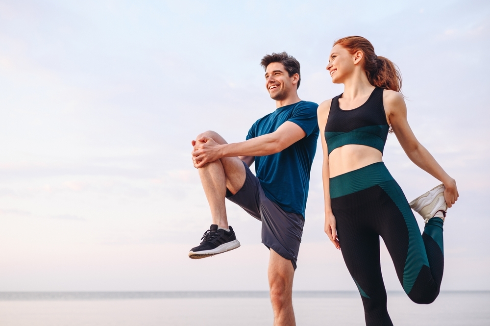 Lower couple young two friend strong sporty sportswoman sportsman woman man in sport clothes warm up training do stretch exercise on sand sea ocean beach outdoor jog on seaside in summer day morning Lower couple young two friend strong sporty sportswoman sportsman woman man in sport clothes warm up training do stretch exercise on sand sea ocean beach outdoor jog on seaside in summer day morning