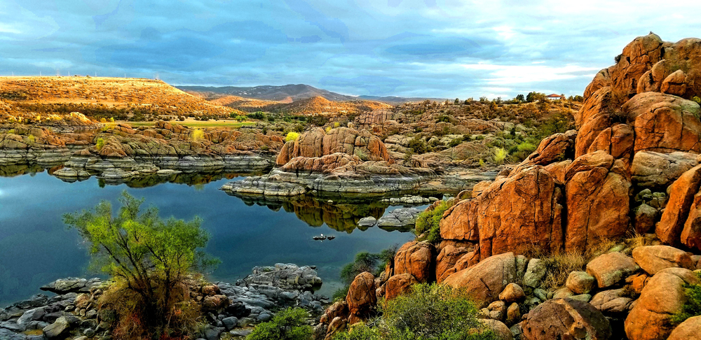 Sunset after late summer storm at Lake Watson, Prescott, Arizona with golden rocks over still blue skies with sky reflection