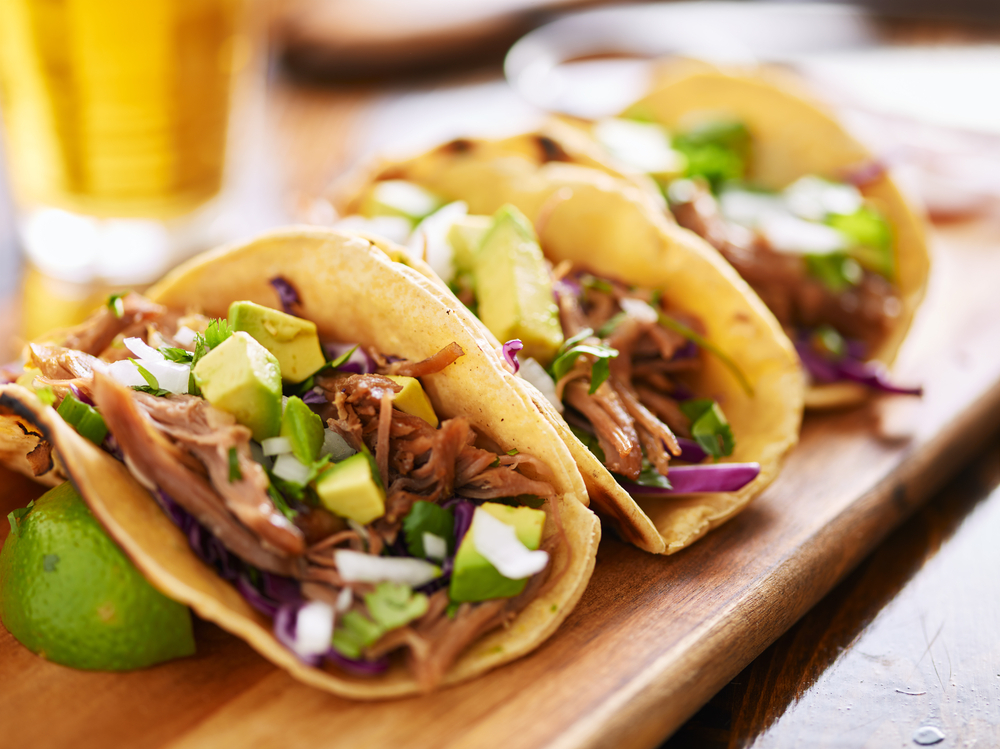 three pork carnitas street tacos in yellow corn tortilla with avocado, onion, cilantro and cabbage