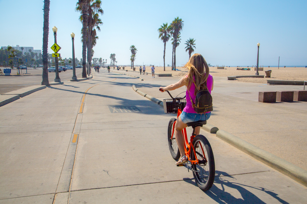 Young beautiful girl riding a bike down the Venice beach in Los Angeles. Californian dreaming.