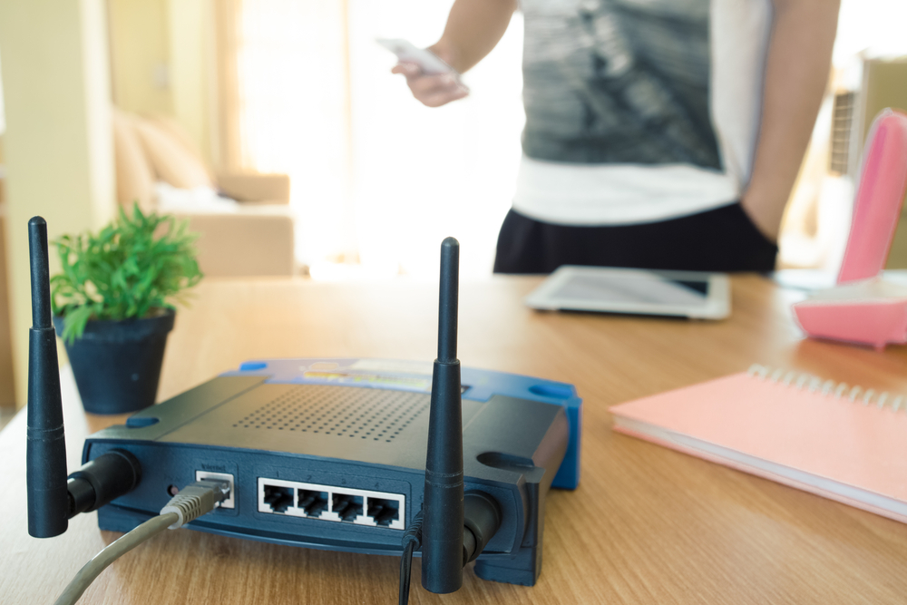 closeup of a wireless router and a young man using a smartphone on living room at home with a window in the background