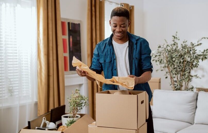 A young man unpacks in a living room after a move.