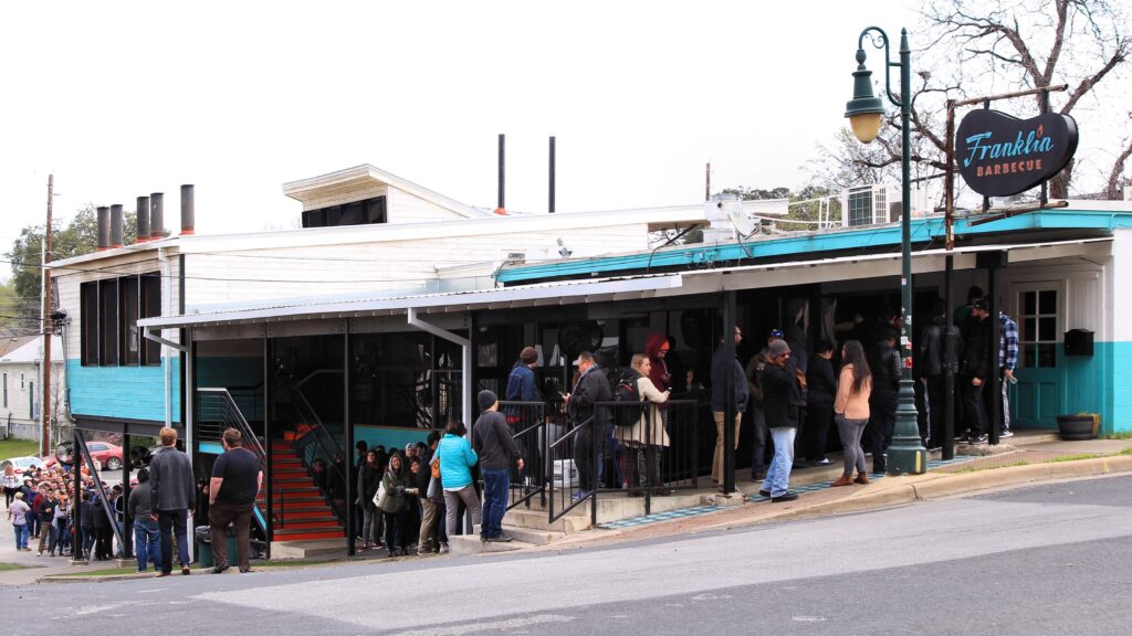 Long line of people in the front of a barbecue restaurant with the sign Franklin Barbecue.