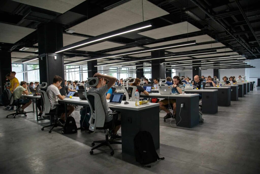 Rows of desks with multiple people working on them with their computers.