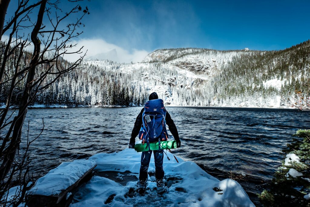 Man hiking at a snowy Rocky Mountain National Park with a lake and a mountain in the background