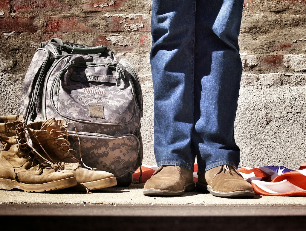 Military boots and backpack plus a US flag, lying on the floor next to a military retiree.
